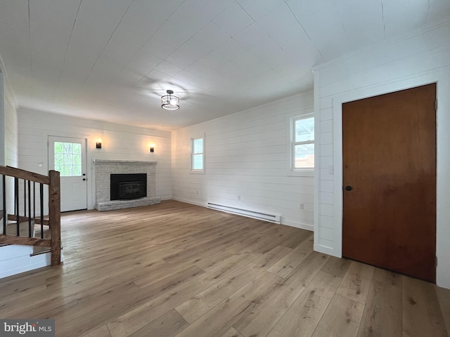unfurnished living room featuring crown molding, a fireplace, a baseboard heating unit, stairs, and light wood-style flooring