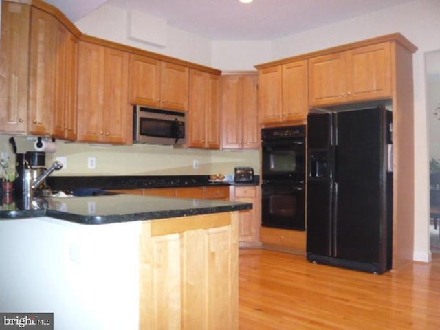 kitchen with dark countertops, a sink, light wood-style flooring, a peninsula, and black appliances
