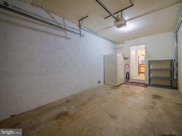 garage featuring freestanding refrigerator, concrete block wall, and a garage door opener
