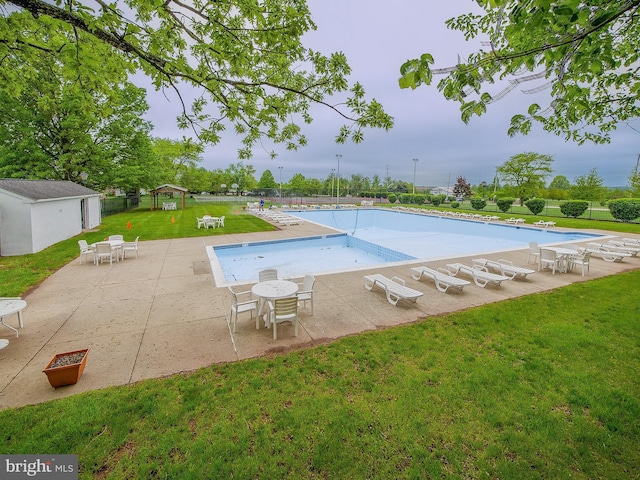 community pool featuring fence, a patio, an outdoor structure, and a lawn