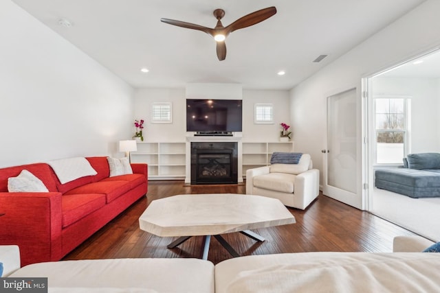 living room featuring ceiling fan, visible vents, wood finished floors, a glass covered fireplace, and recessed lighting
