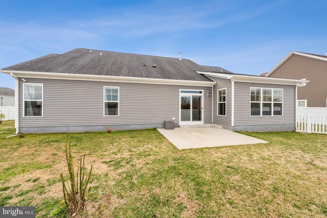 back of property with a lawn, a patio area, fence, and roof with shingles