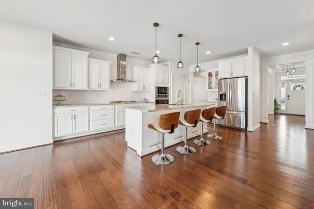 kitchen with wall chimney range hood, decorative backsplash, a breakfast bar area, stainless steel appliances, and dark wood-type flooring