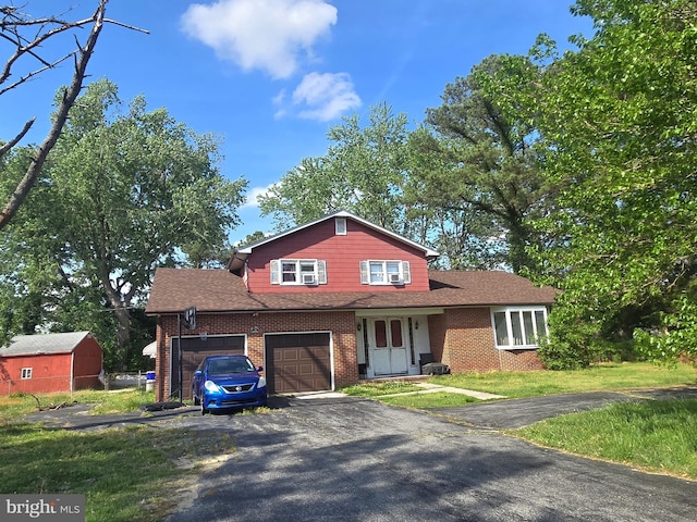 split level home with a garage, aphalt driveway, a front yard, brick siding, and a shingled roof