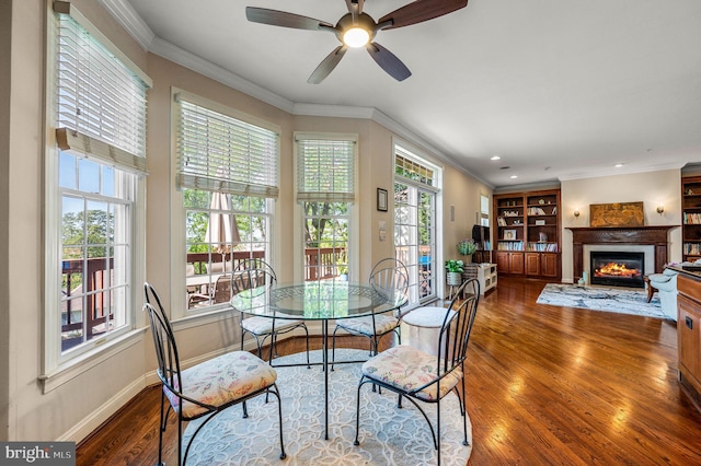 dining area with wood finished floors, a glass covered fireplace, baseboards, ornamental molding, and a ceiling fan