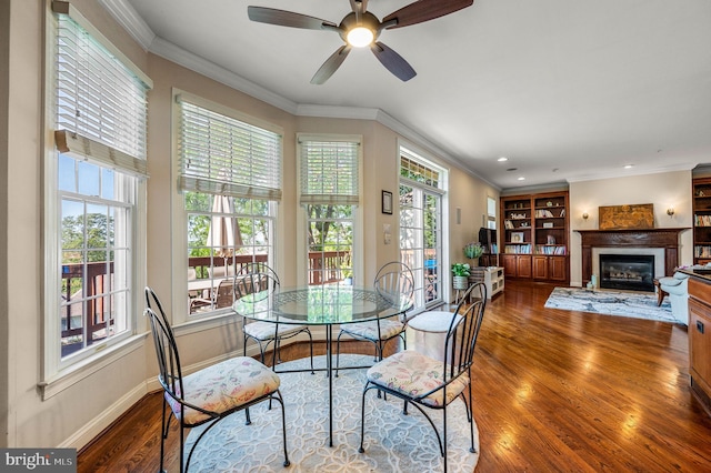 dining space featuring wood finished floors, a glass covered fireplace, baseboards, ornamental molding, and ceiling fan