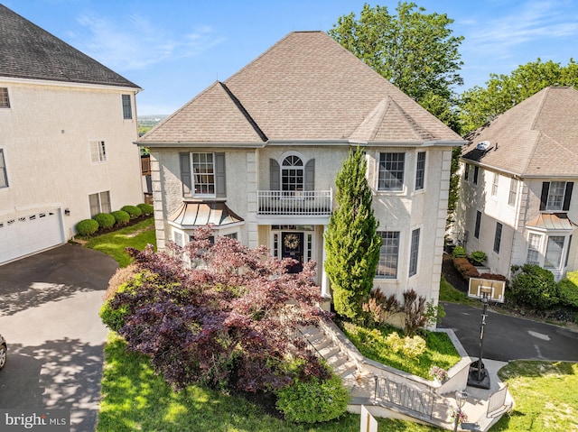 view of front facade with a balcony, roof with shingles, asphalt driveway, and stucco siding