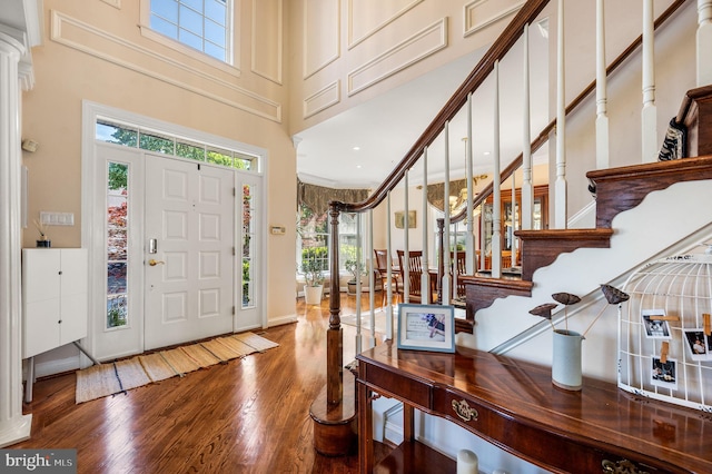 foyer featuring wood finished floors, a high ceiling, stairs, ornate columns, and baseboards