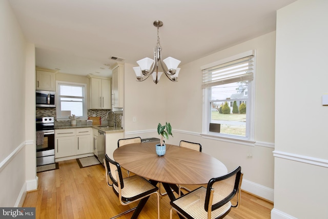 dining area featuring visible vents, light wood-style flooring, baseboards, and a notable chandelier