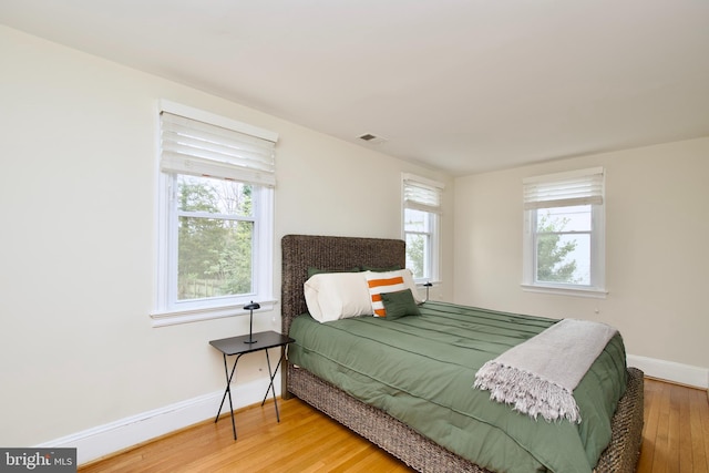 bedroom with baseboards, visible vents, and wood finished floors