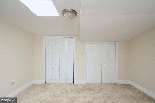unfurnished bedroom featuring baseboards, carpet flooring, two closets, and a skylight