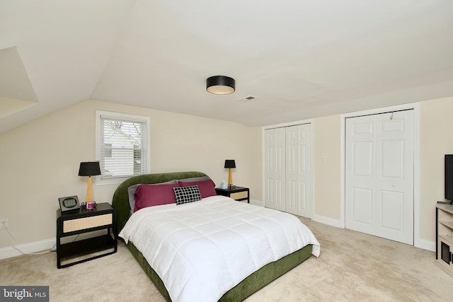 bedroom featuring visible vents, vaulted ceiling, baseboards, multiple closets, and light carpet