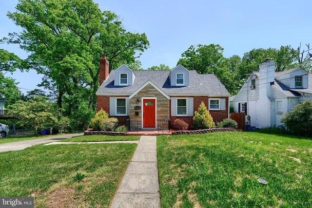 cape cod house featuring brick siding, a front lawn, roof with shingles, and a chimney