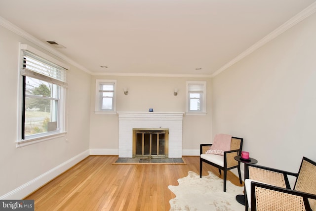 sitting room with baseboards, crown molding, light wood-style flooring, and a brick fireplace