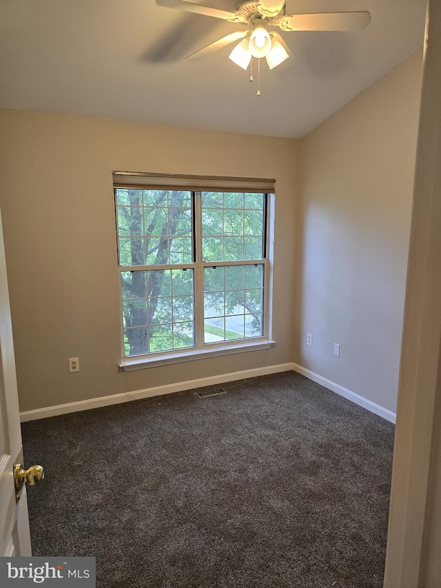 unfurnished room with healthy amount of natural light, dark colored carpet, a ceiling fan, and baseboards