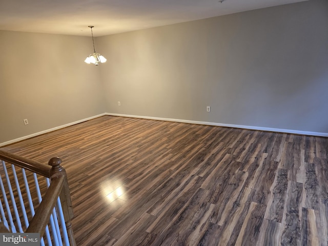 empty room featuring dark wood-type flooring, a chandelier, and baseboards