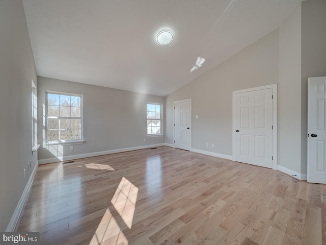 unfurnished living room with light wood-style floors, high vaulted ceiling, and baseboards