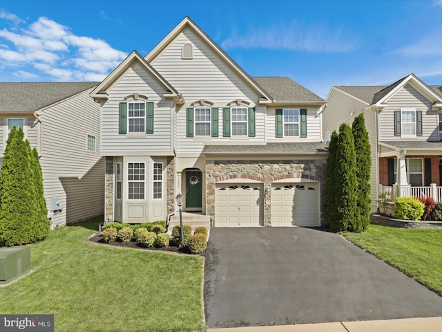 traditional-style home featuring stone siding, a garage, aphalt driveway, a front yard, and roof with shingles