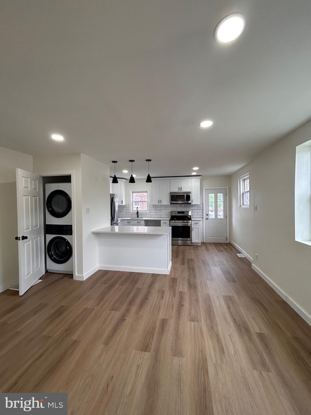 kitchen featuring a peninsula, stainless steel appliances, stacked washer / dryer, light countertops, and white cabinets