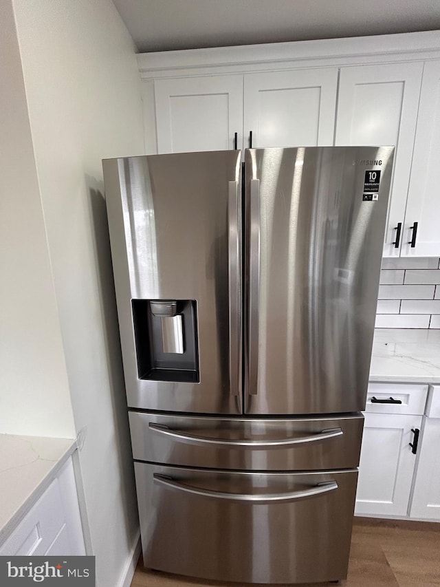 interior details featuring white cabinets, light stone counters, wood finished floors, and stainless steel refrigerator with ice dispenser