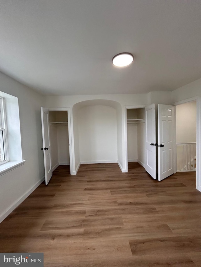 unfurnished bedroom with baseboards, light wood-style flooring, and two closets