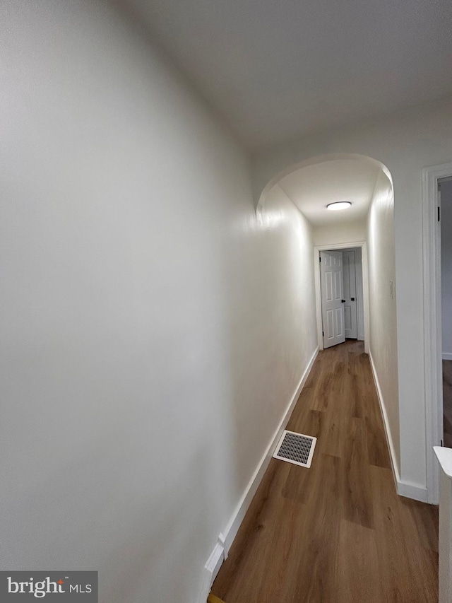 hallway with arched walkways, baseboards, visible vents, and wood finished floors