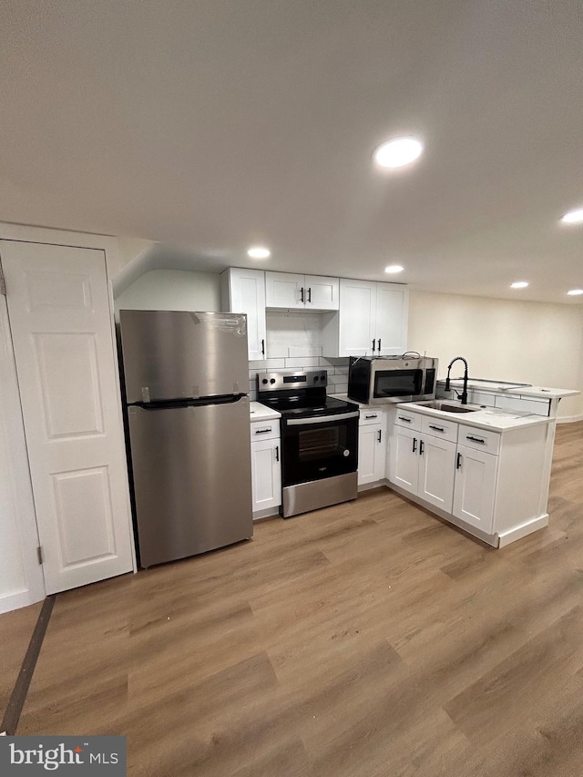 kitchen with a peninsula, light wood-style flooring, a sink, white cabinets, and appliances with stainless steel finishes