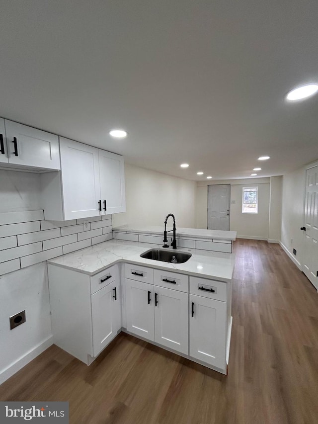 kitchen featuring a sink, a peninsula, white cabinets, and wood finished floors