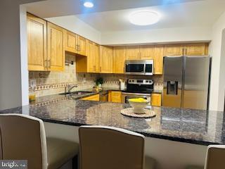 kitchen featuring appliances with stainless steel finishes, dark stone counters, a peninsula, recessed lighting, and backsplash