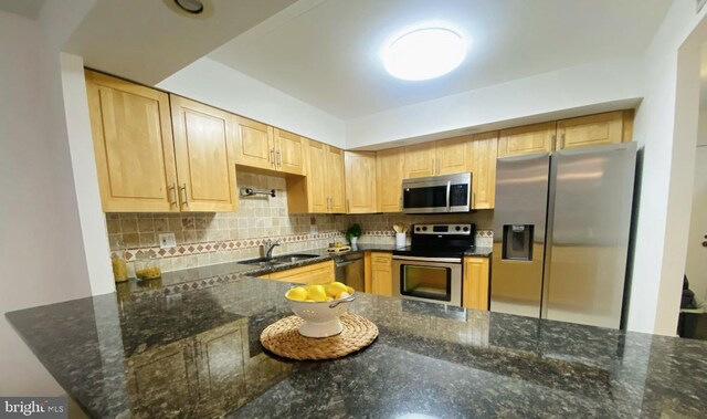 kitchen with decorative backsplash, a sink, dark stone countertops, light brown cabinets, and stainless steel appliances