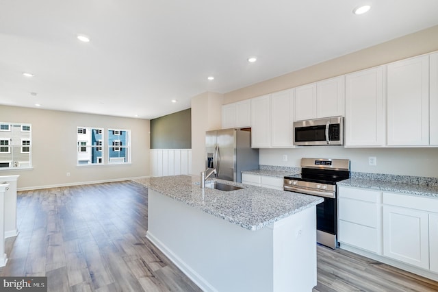 kitchen featuring appliances with stainless steel finishes, a sink, light wood-style floors, white cabinetry, and an island with sink