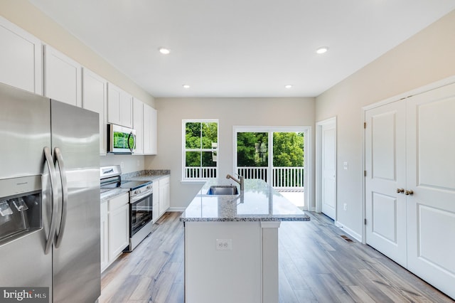 kitchen with a kitchen island with sink, white cabinetry, light stone counters, a sink, and appliances with stainless steel finishes