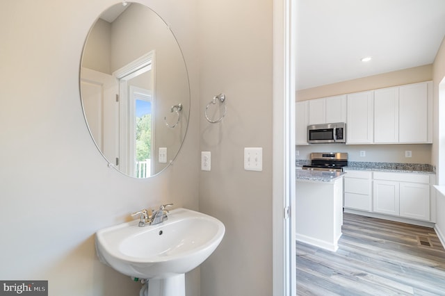 bathroom featuring recessed lighting, a sink, and wood finished floors