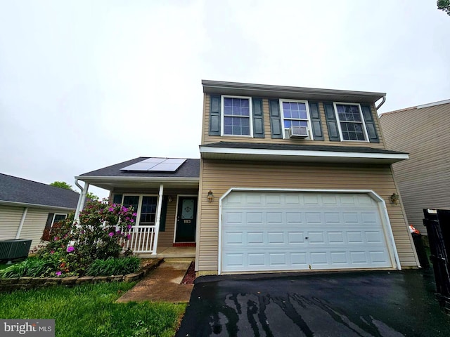 traditional-style home with a garage, cooling unit, solar panels, a porch, and driveway
