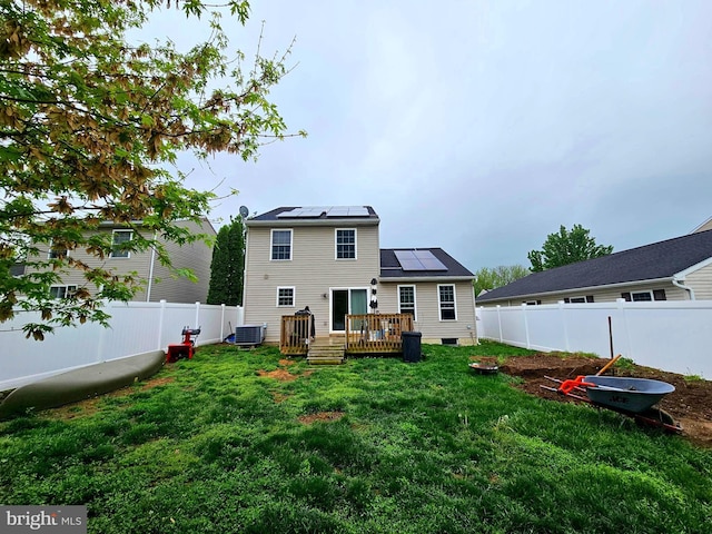 back of house with central air condition unit, roof mounted solar panels, a fenced backyard, and a yard