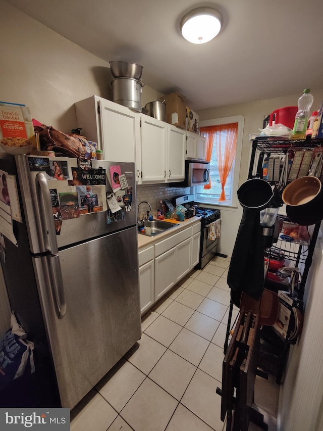 kitchen with light tile patterned floors, white cabinets, a sink, appliances with stainless steel finishes, and backsplash
