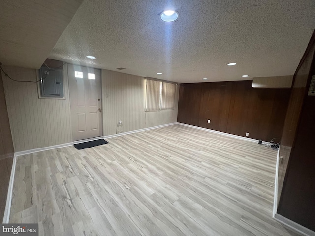 finished below grade area with baseboards, a textured ceiling, light wood finished floors, and electric panel