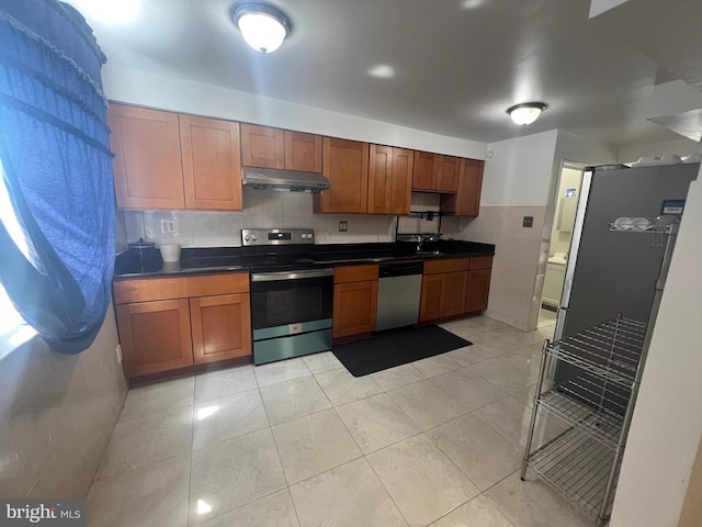 kitchen with dark countertops, appliances with stainless steel finishes, brown cabinets, a sink, and under cabinet range hood