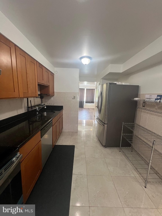 kitchen featuring dark countertops, a sink, brown cabinetry, stainless steel appliances, and tile walls