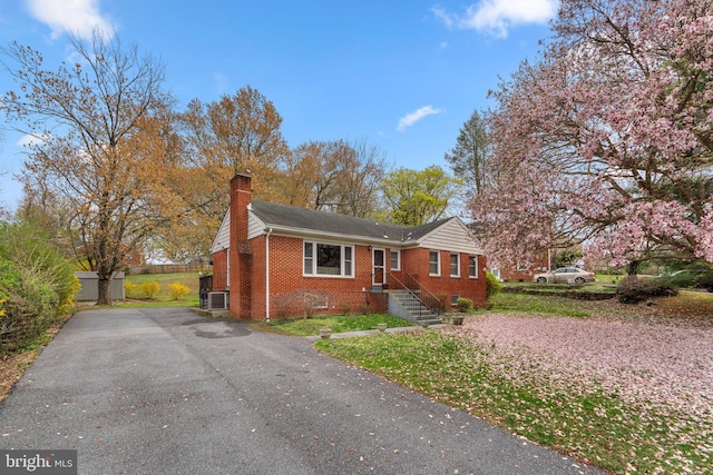 view of front of house with fence, a chimney, brick siding, and driveway