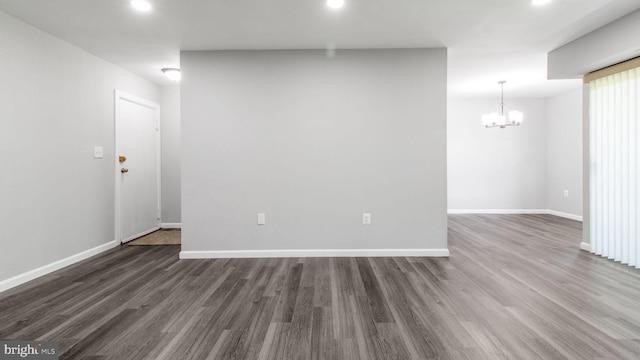 empty room featuring an inviting chandelier, recessed lighting, baseboards, and dark wood-type flooring