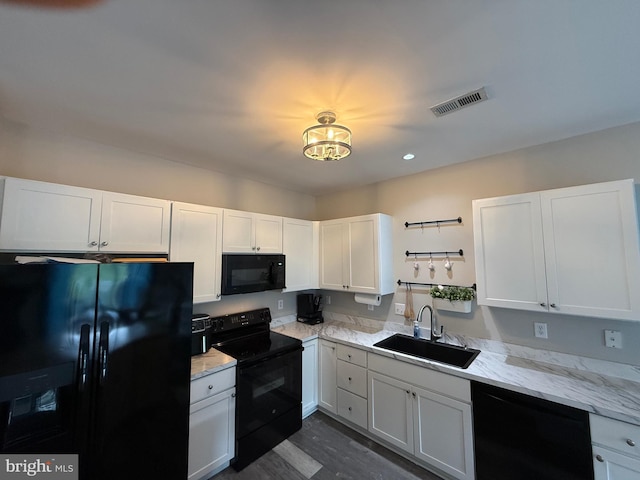 kitchen featuring visible vents, light stone countertops, white cabinets, a sink, and black appliances