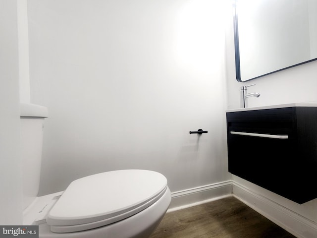 half bath with baseboards, vanity, toilet, and wood finished floors
