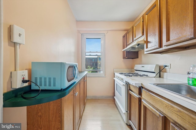 80 W Baltimore Ave Unit C507, Lansdowne, PA 19050 - kitchen with white gas range oven, under cabinet range hood, brown cabinetry, light wood-type flooring, and light countertops