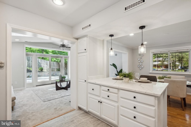 kitchen with healthy amount of natural light, light stone counters, a ceiling fan, white cabinets, and recessed lighting