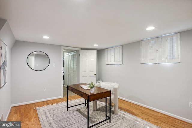 office featuring wood finished floors, baseboards, stacked washing machine and dryer, and recessed lighting