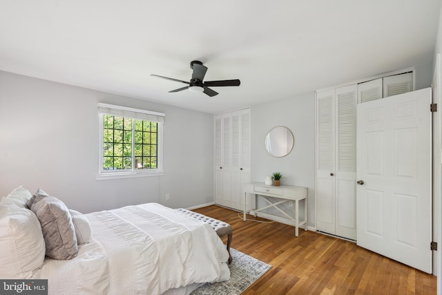bedroom featuring multiple closets, wood finished floors, a ceiling fan, and baseboards