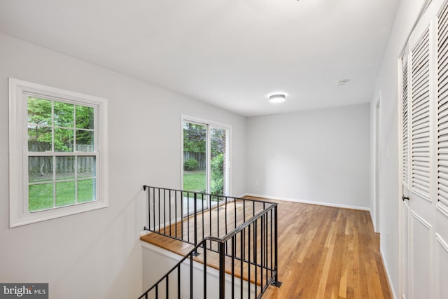 corridor featuring an upstairs landing, light wood finished floors, and baseboards