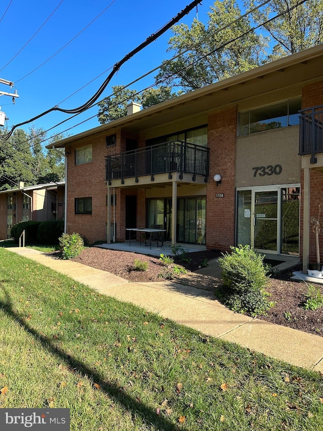 rear view of house with brick siding, a lawn, and a balcony