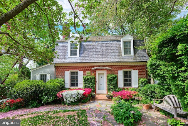 view of front of house with a high end roof, a chimney, mansard roof, and brick siding